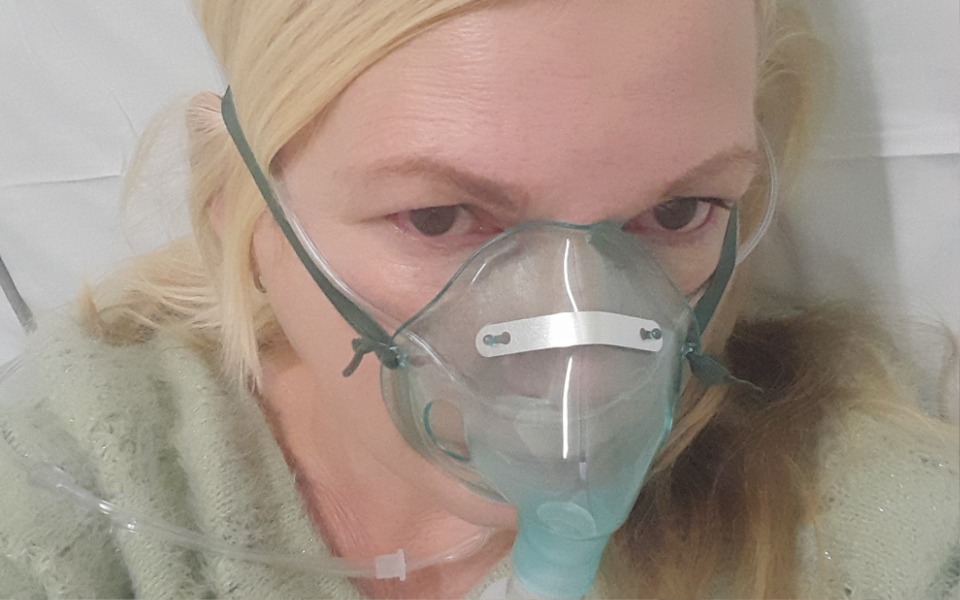 
        Kobieta w szpitalu z maską tlenową, wygląda na zmartwioną.
    