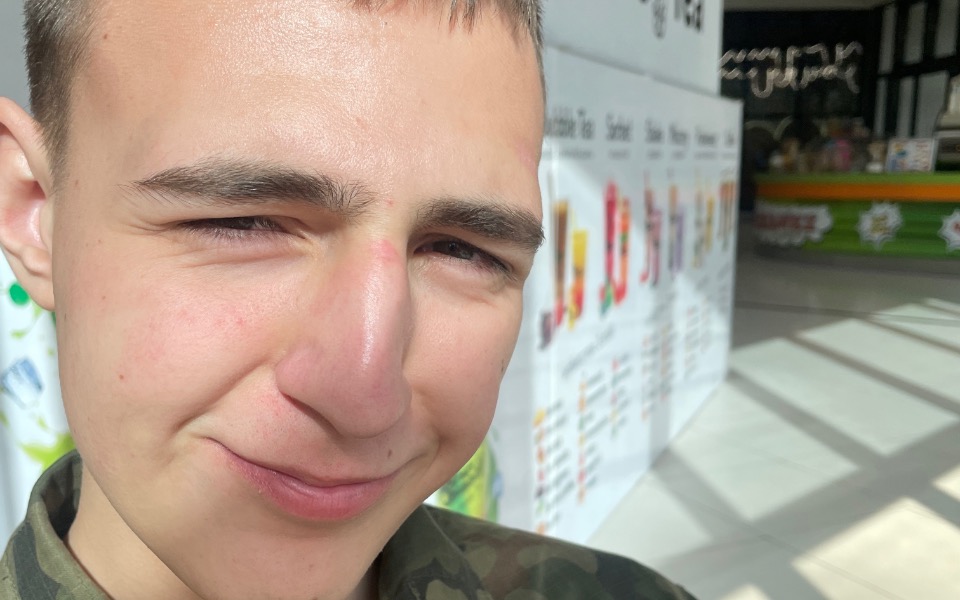 
        Młody mężczyzna z uśmiechem, w tle kolorowe plakaty.
    