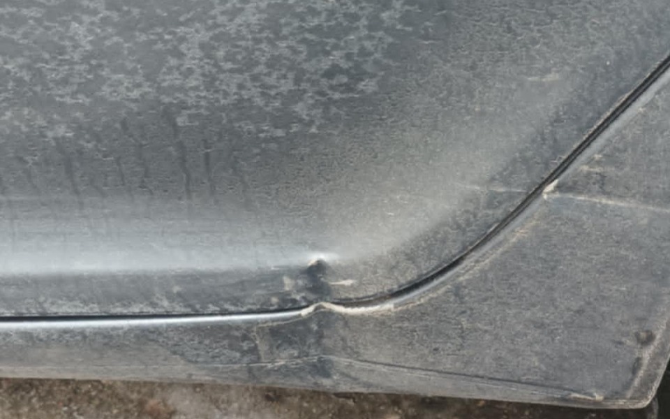 
        Zbliżenie na zarysowany bok samochodu, pokryty kurzem.
    