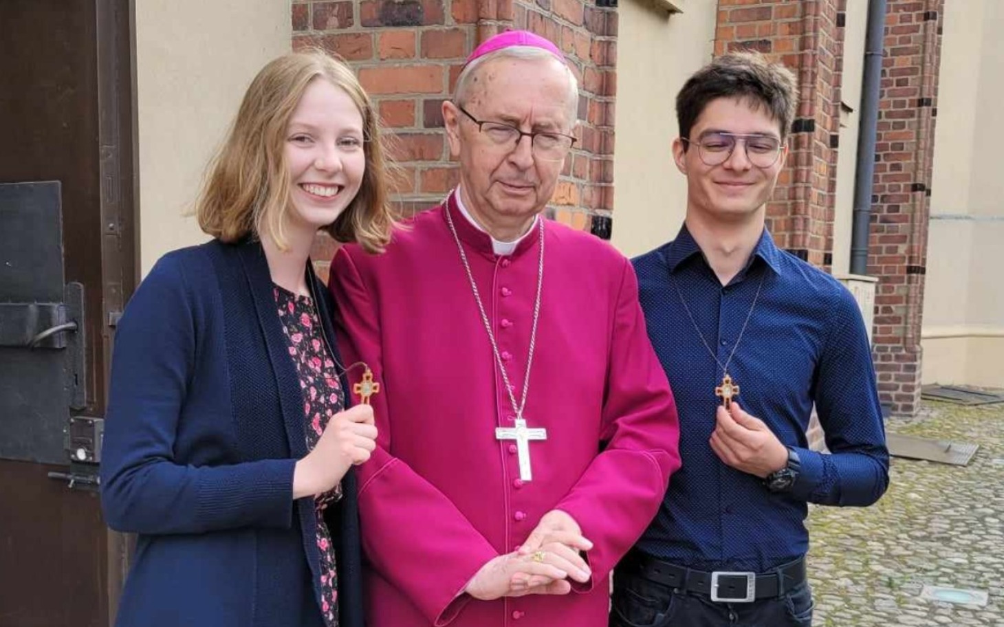 Biskup z młodzieżą, trzymający krzyże w rękach.