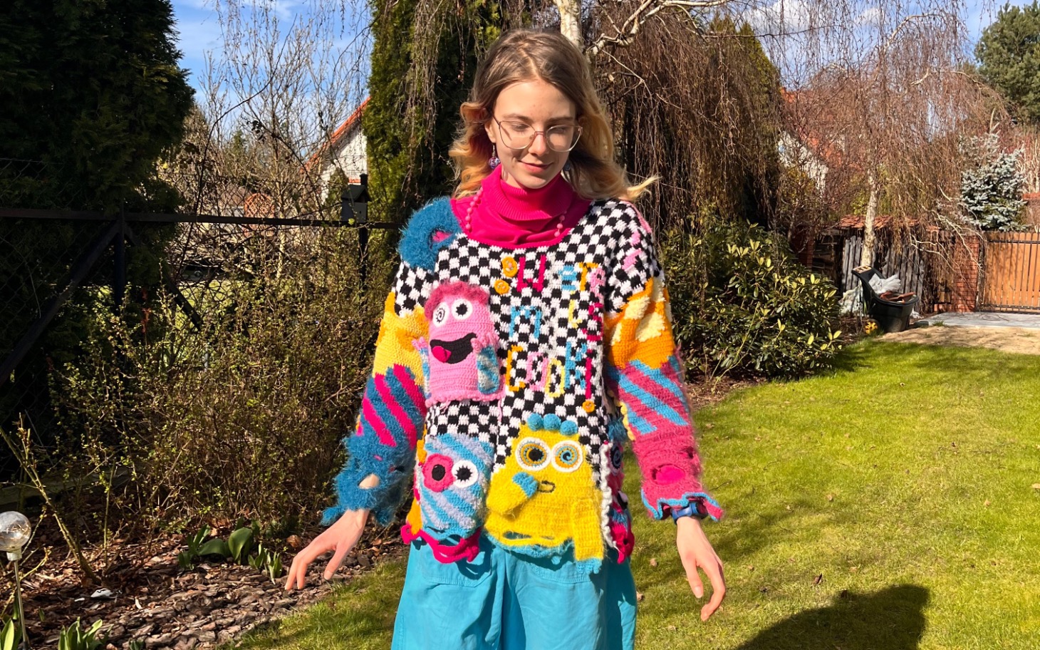 
        Młoda kobieta w kolorowym swetrze na tle ogrodu.
    