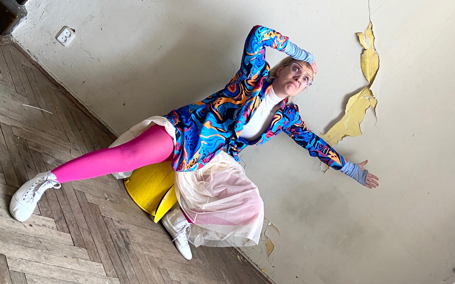 Osoba w kolorowym stroju pozująca w zniszczonym pomieszczeniu.