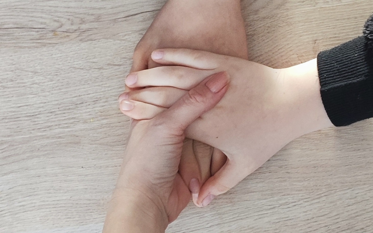 
        Ręce różnych osób trzymające się nawzajem na stole.
    