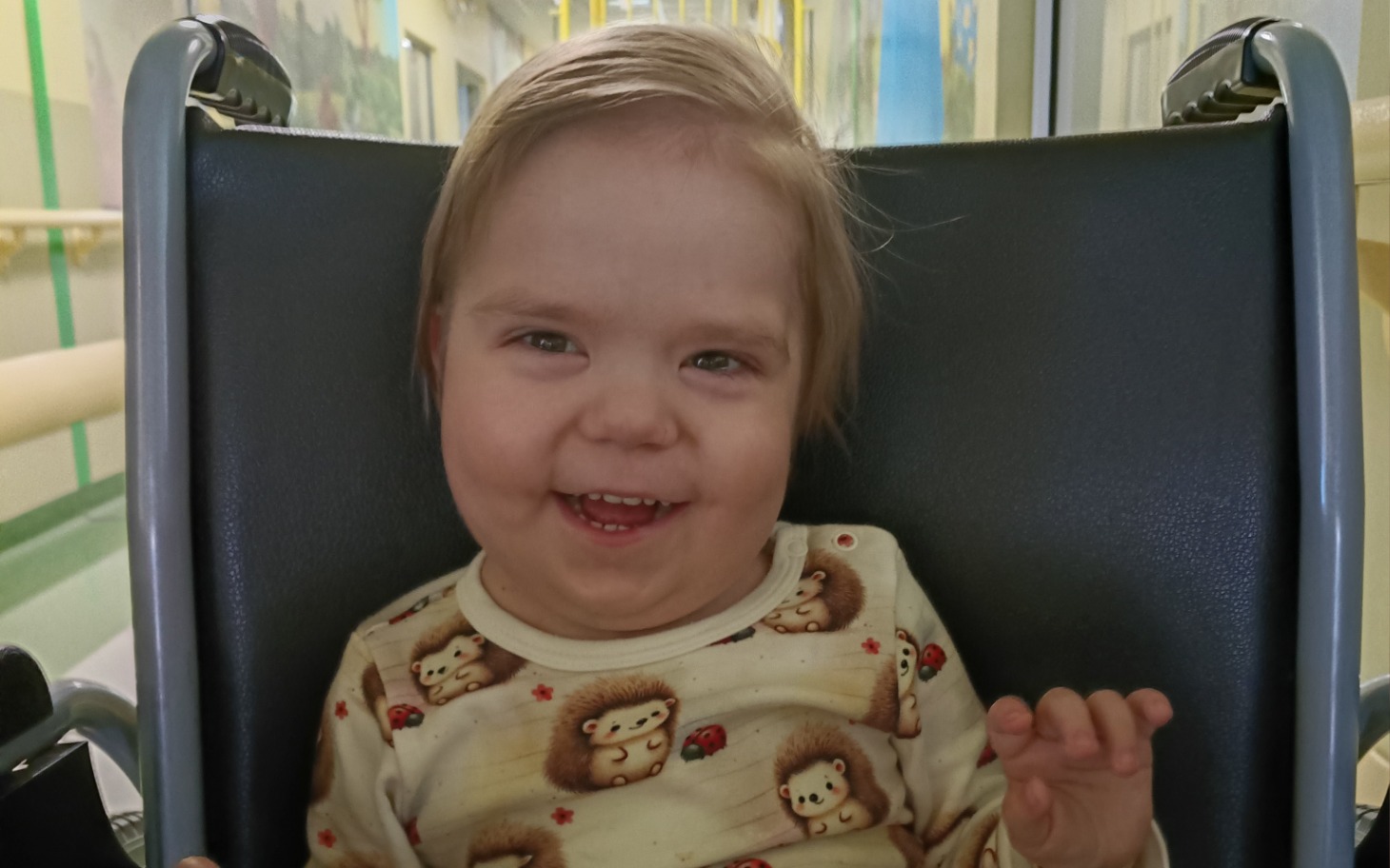 
        Uśmiechnięta dziewczynka w wózku, w kolorowej piżamie.
    