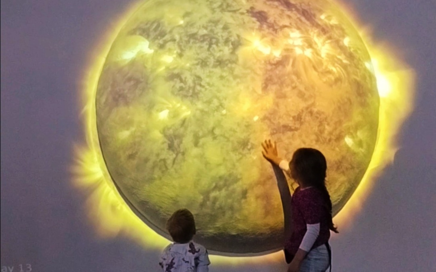 
        Dzieci dotykające interaktywnej, świetlnej planety.
    