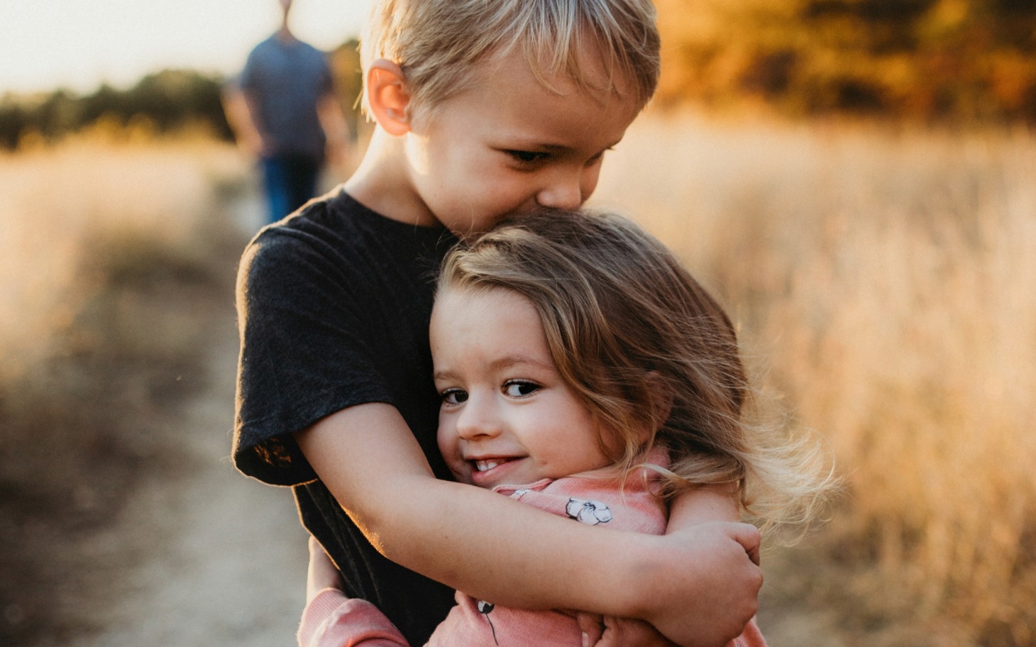 
        Dzieci przytulające się na tle złotych pól.
    