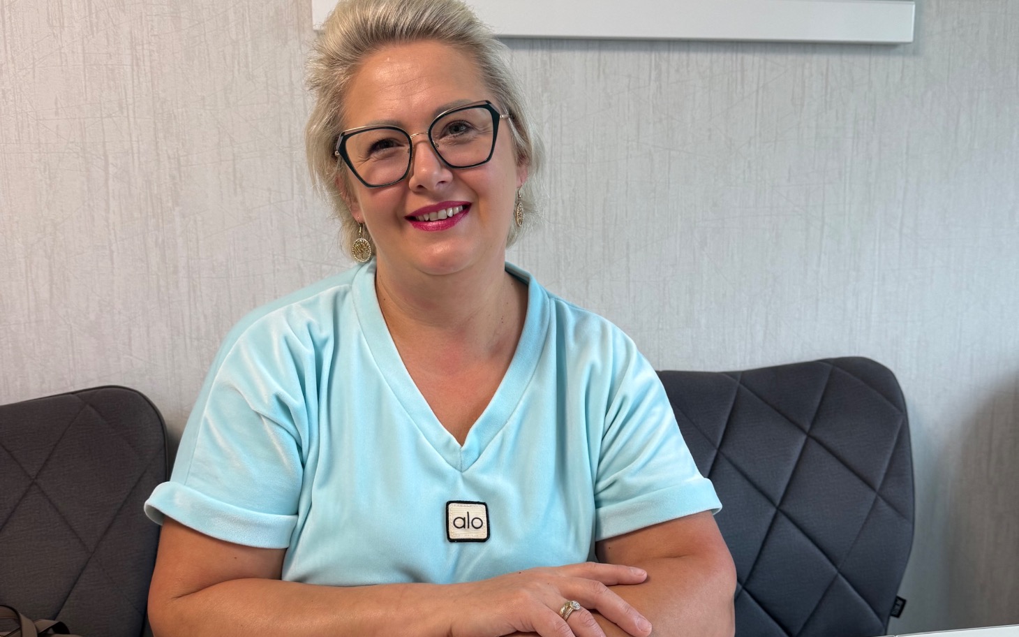 Uśmiechnięta kobieta w jasnym błękitnym topie, siedzi na sofie