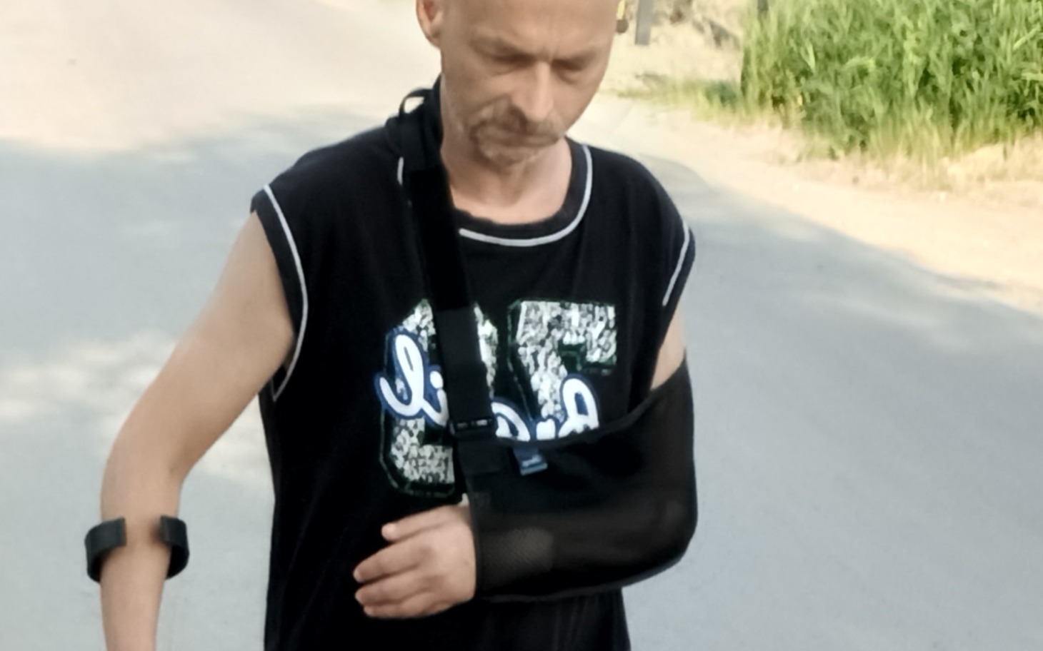 
        Mężczyzna z unieruchomioną ręką, spacerujący po drodze.
    