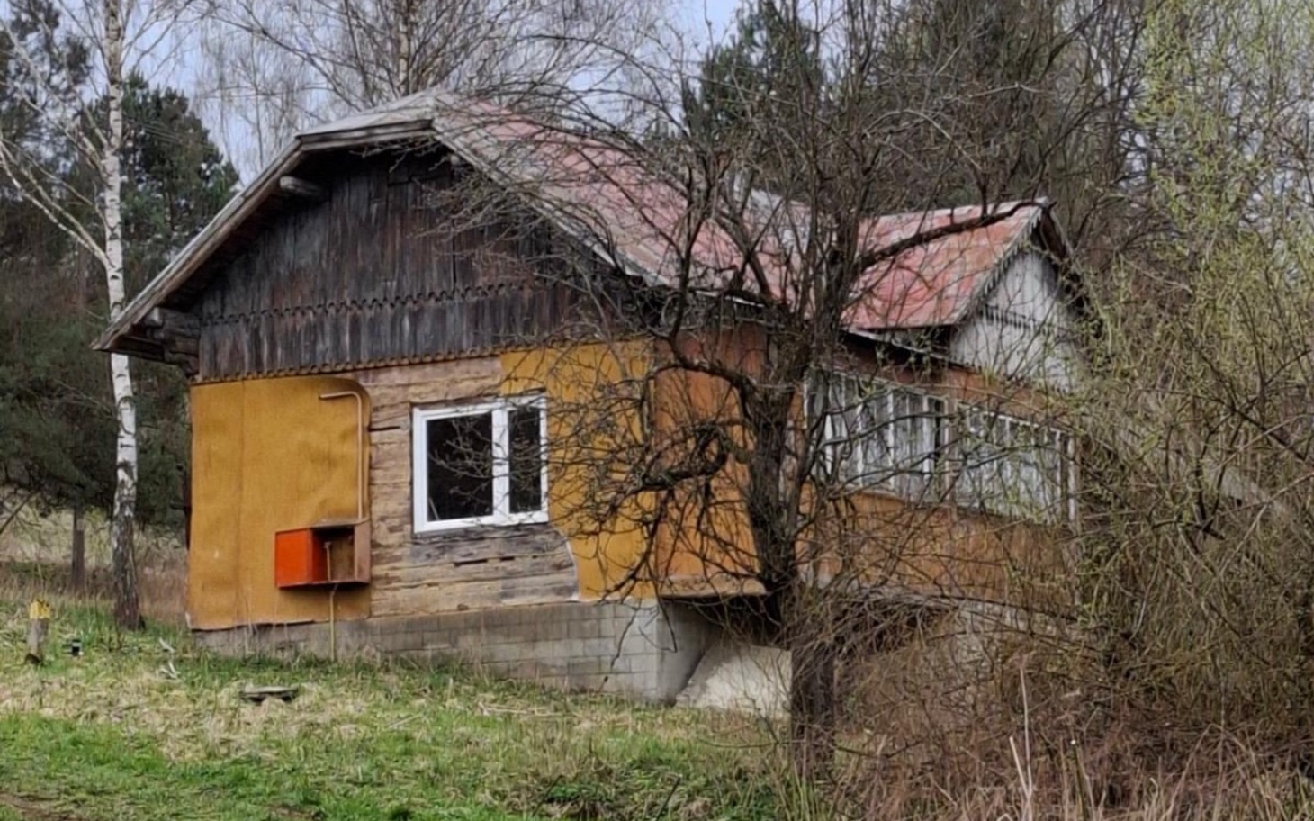 
        Stary dom z drewnianą elewacją otoczony drzewami.
    