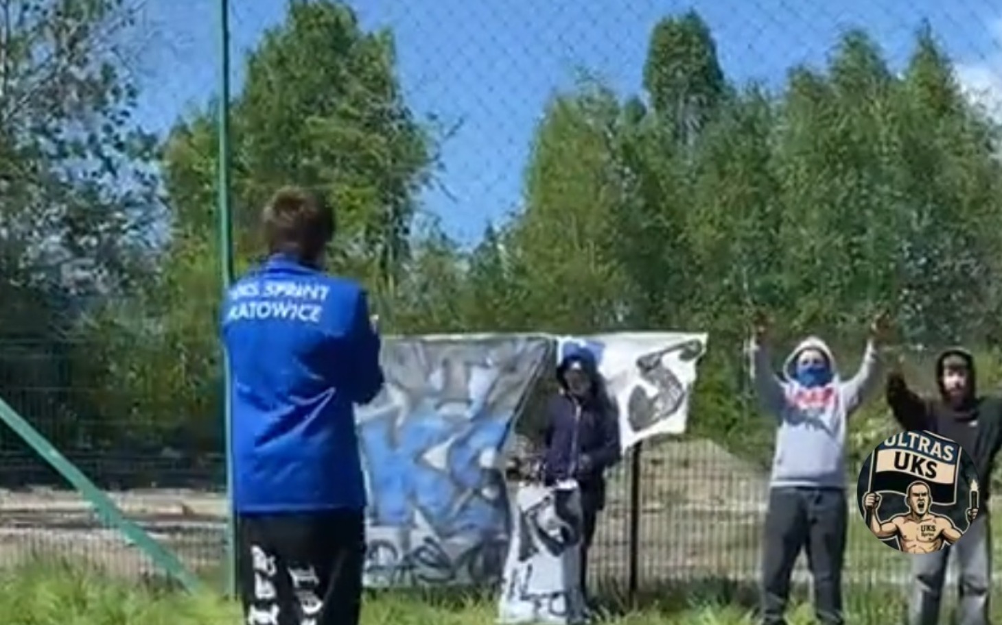 
        Grupa kibiców na boisku z transparentem.
    