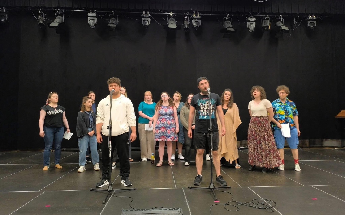 
        Grupa ludzi na scenie podczas próby teatralnej.
    