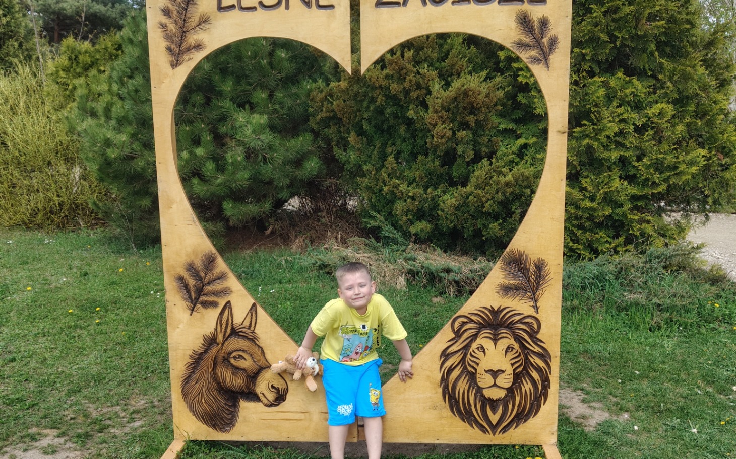 
        Chłopiec pozujący przy drewnianej dekoracji w kształcie serca.
    