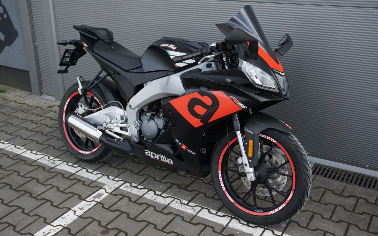 
        Motocykl sportowy marki Aprilia na parkingu.
    