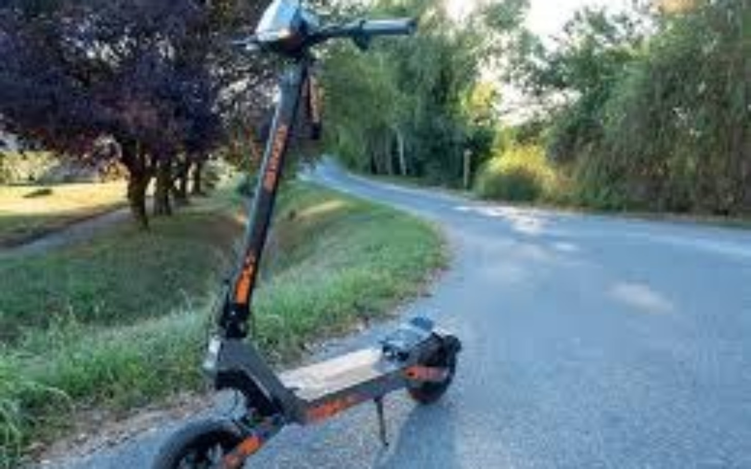 
        Elektryczna hulajnoga na drodze w otoczeniu zieleni.
    