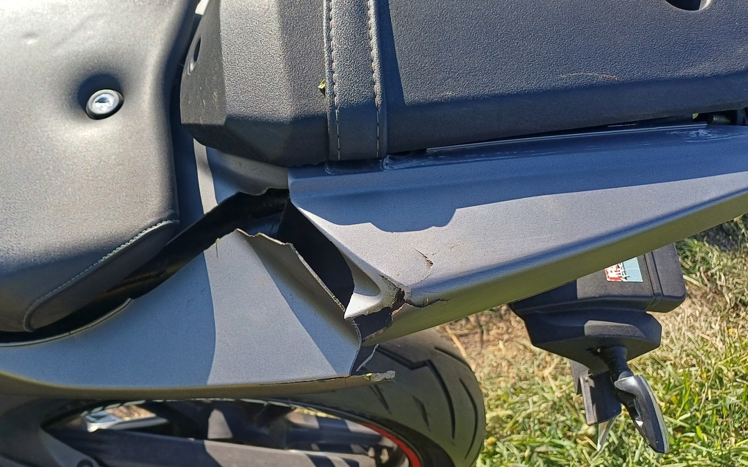 
        Uszkodzona część motocykla, widoczna pęknięta rama.
    