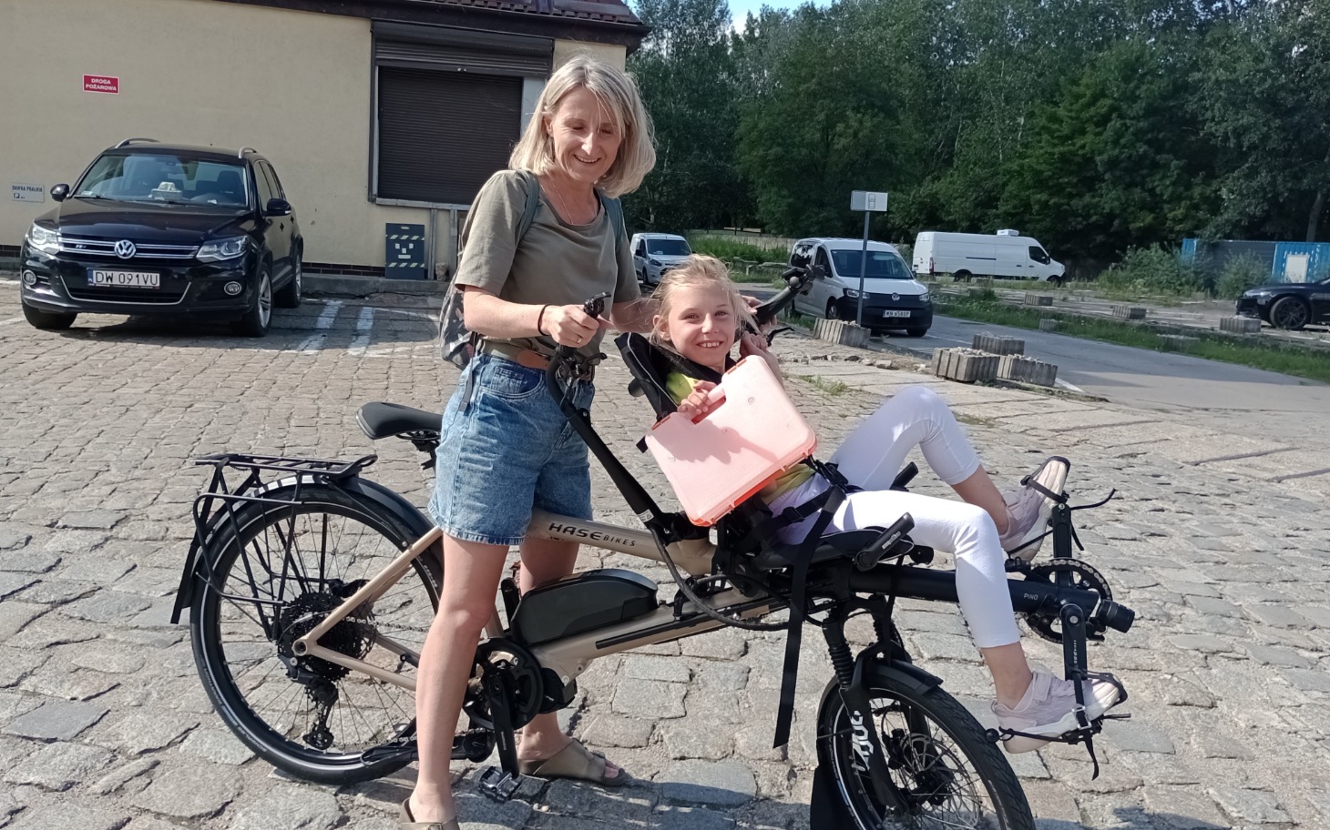 
        Kobieta z dzieckiem na rowerze elektrycznym w słoneczny dzień.
    