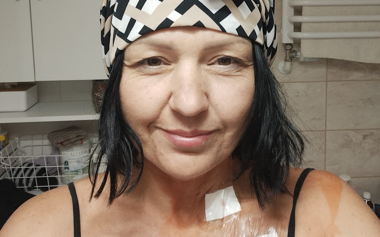
        Kobieta w chustce, uśmiechająca się do kamery.
    