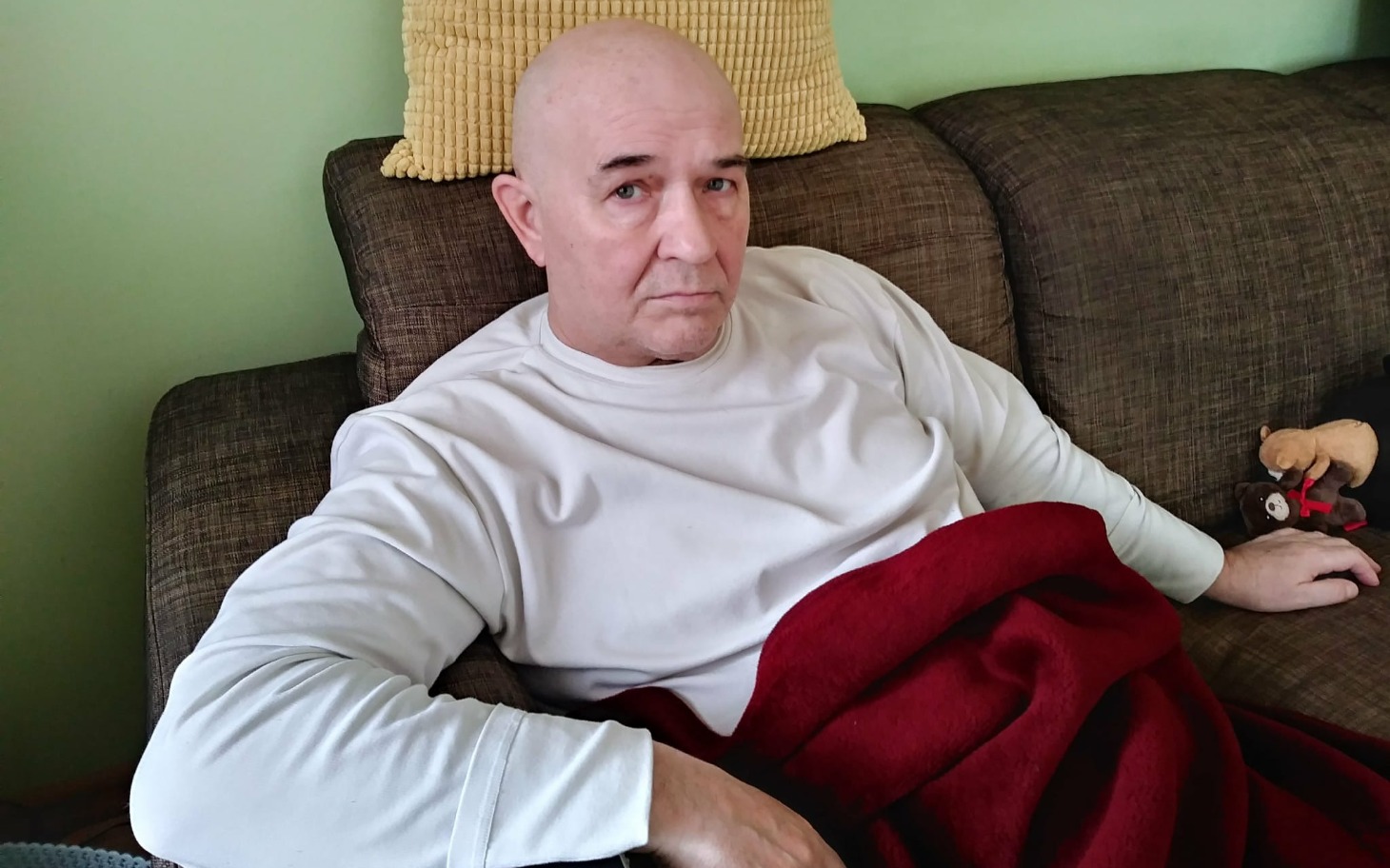 Mężczyzna siedzący na kanapie, przykryty czerwonym kocem.