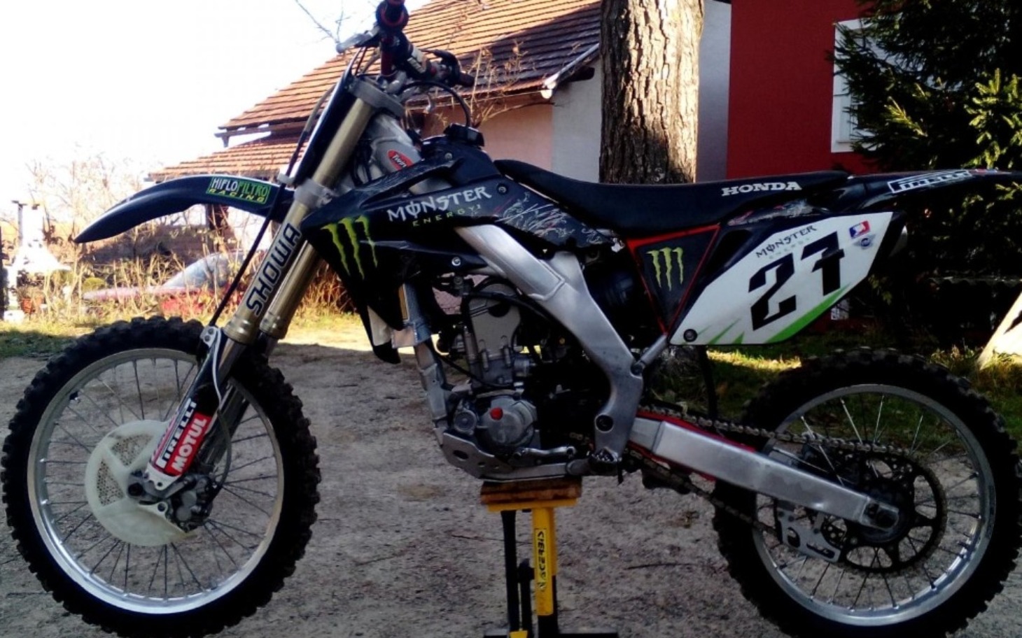 
        Motocykl terenowy marki Honda, stojący na podnośniku.
    