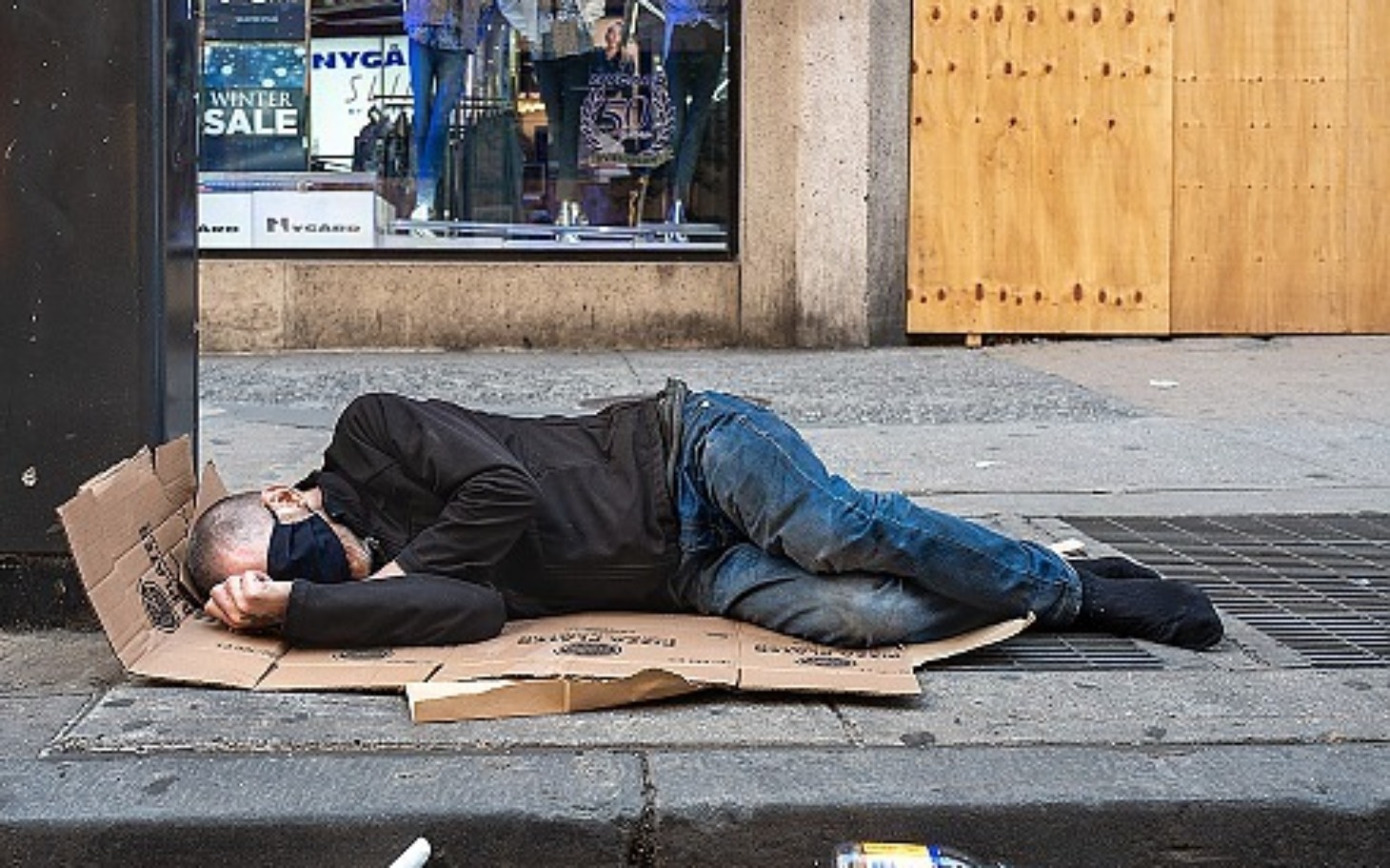 
        Bezdomny mężczyzna śpiący na kartonie na ulicy.
    