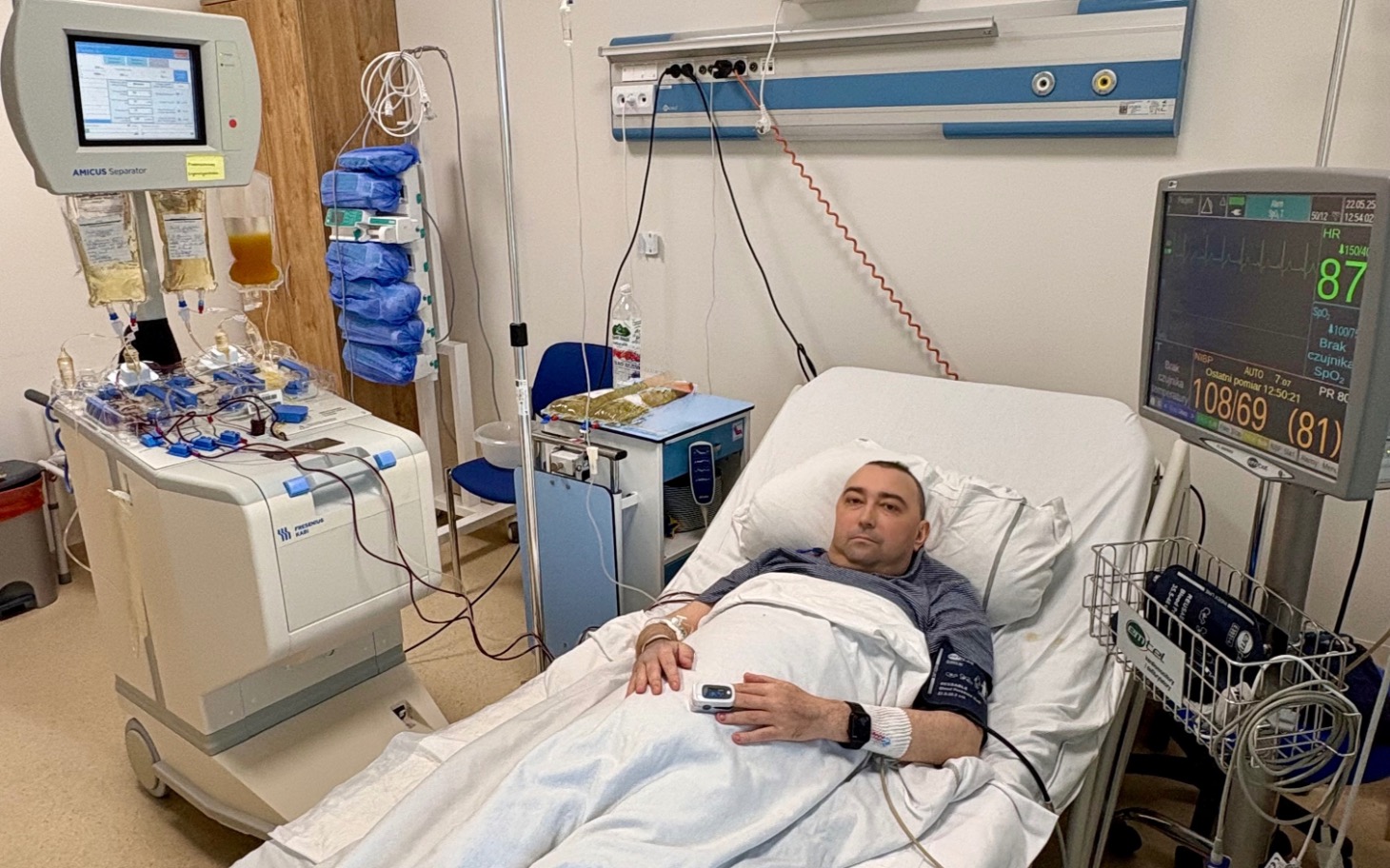 
        Mężczyzna leżący w szpitalnym łóżku, otoczony sprzętem medycznym.
    