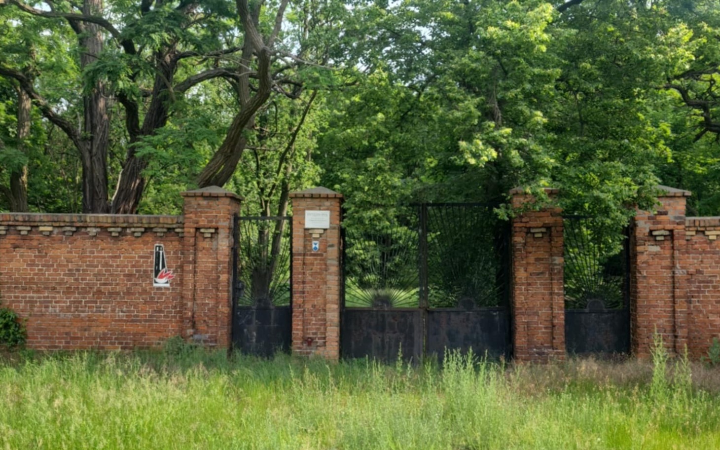 
        Zamknięta brama w parku, otoczona zielenią i drzewami.
    