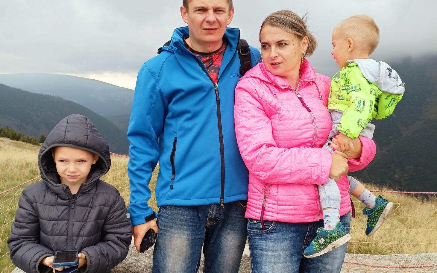 
        Rodzina na górskim szlaku, z dziećmi w kolorowych kurtkach.
    