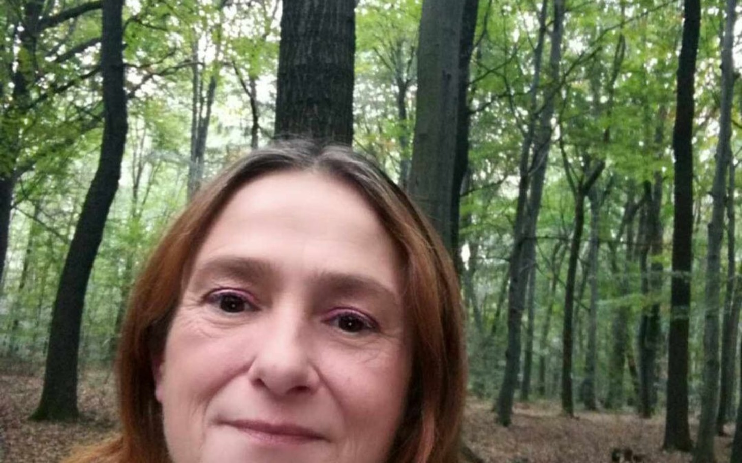 
        Kobieta w lesie, uśmiechająca się do kamery.
    