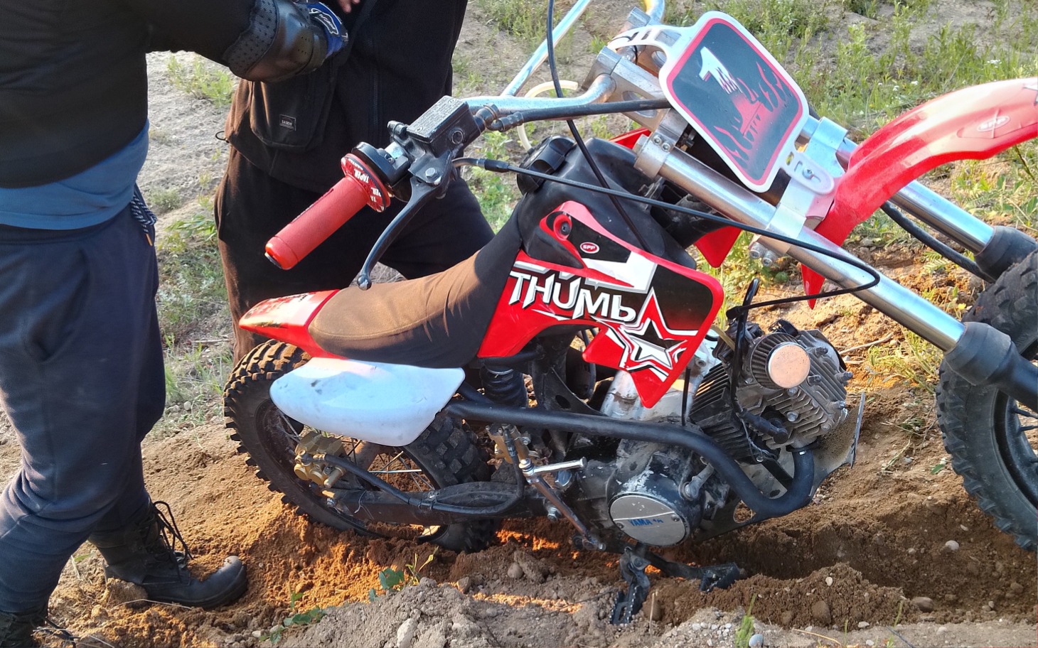 
        Motocykl terenowy w trakcie naprawy na świeżym powietrzu.
    