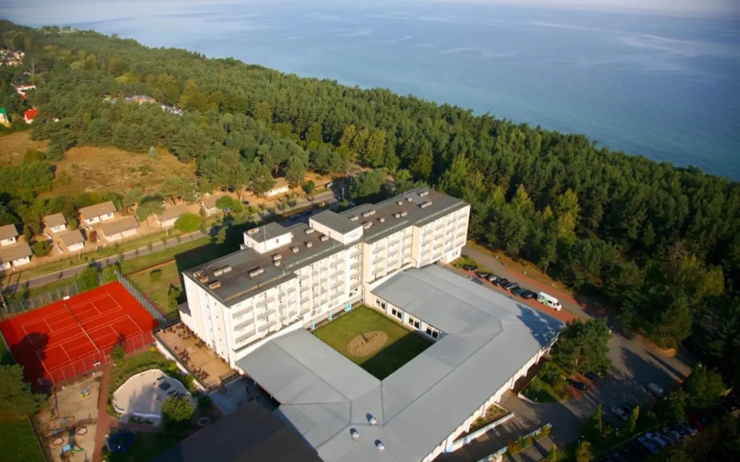 
        Widok na hotel nad morzem, otoczony lasem i zielenią.
    