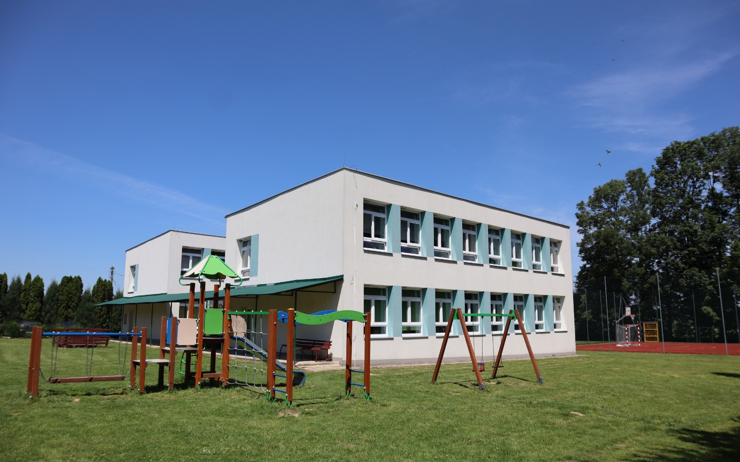 
        Widok na nowoczesną szkołę z placem zabaw.
    