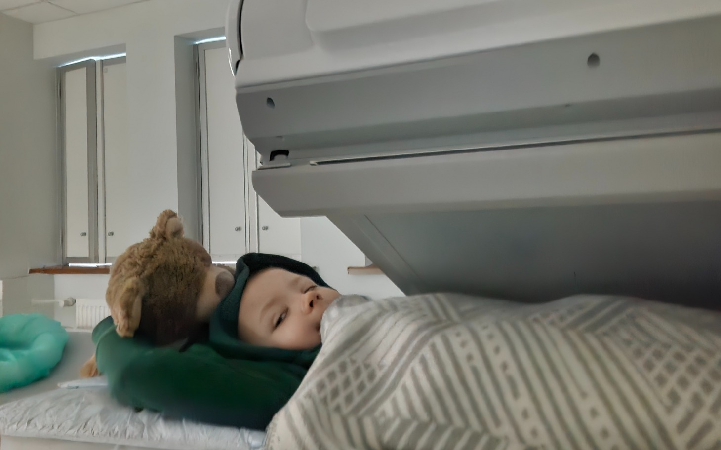 
        Dziecko leży w łóżku z pluszowym misiem.
    