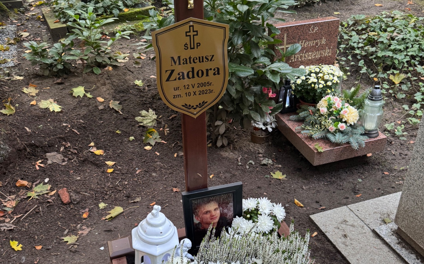 
        Nagrobek Mateusza Zadora z kwiatami i zniczami.
    