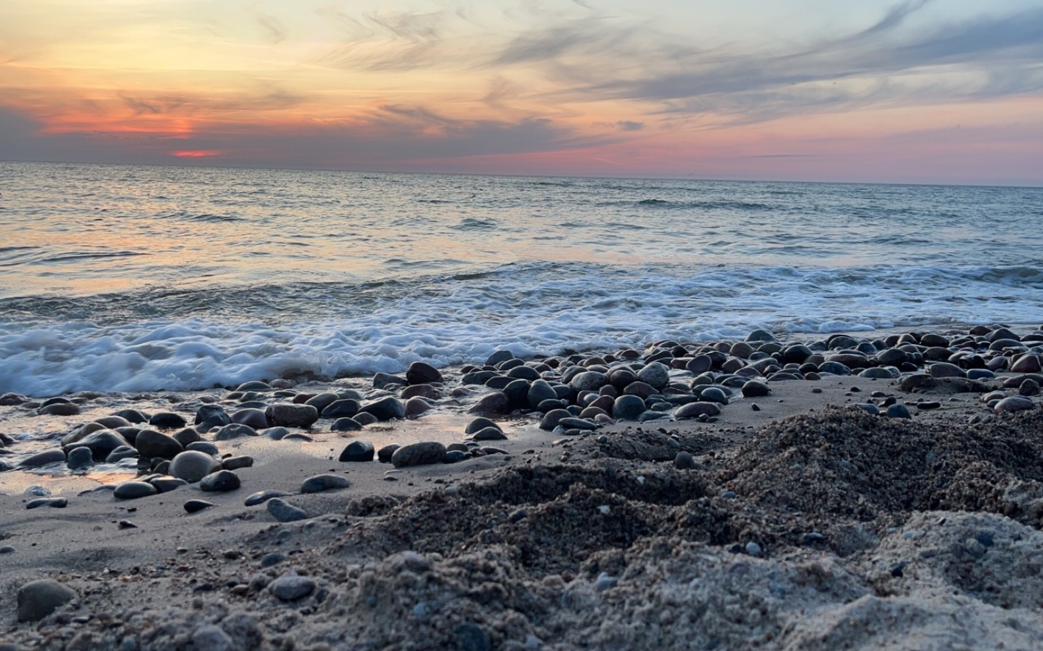 
        Plaża o zachodzie słońca z kamieniami na brzegu.
    