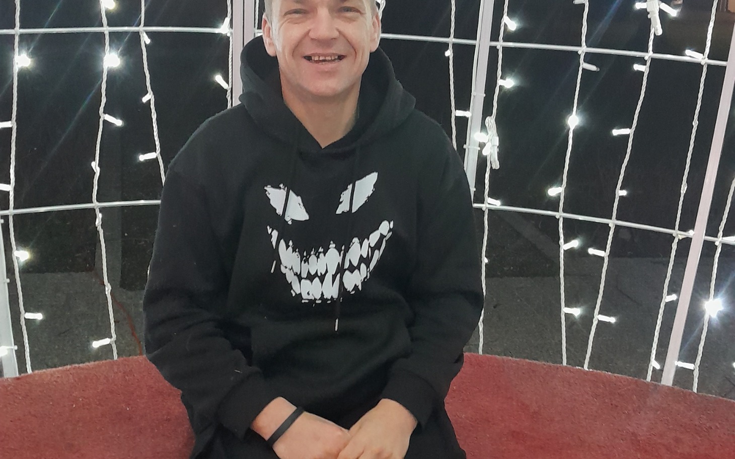 
        Mężczyzna w czarnej bluzie siedzi wśród światełek.
    