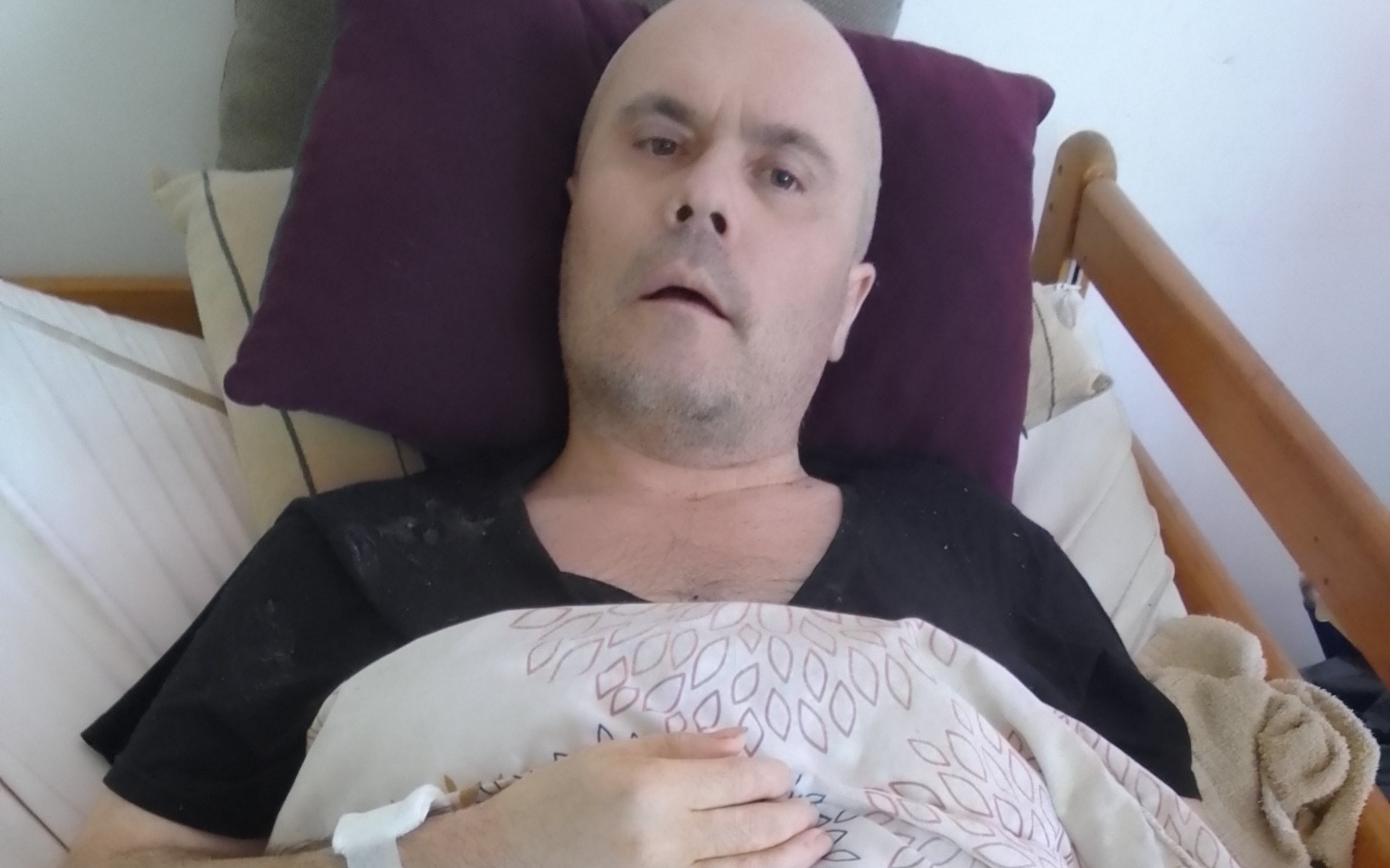 
        Mężczyzna leżący w łóżku, z wyrazem zmęczenia i bólu.
    