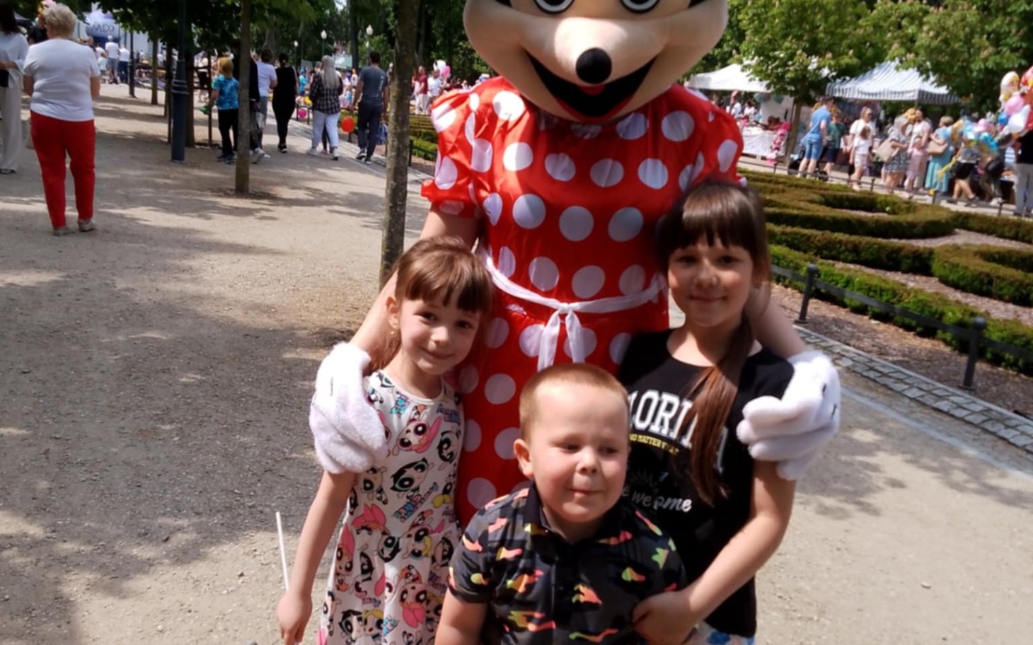 
        Dzieci z uśmiechem pozują z postacią w kostiumie w parku rozrywki.
    