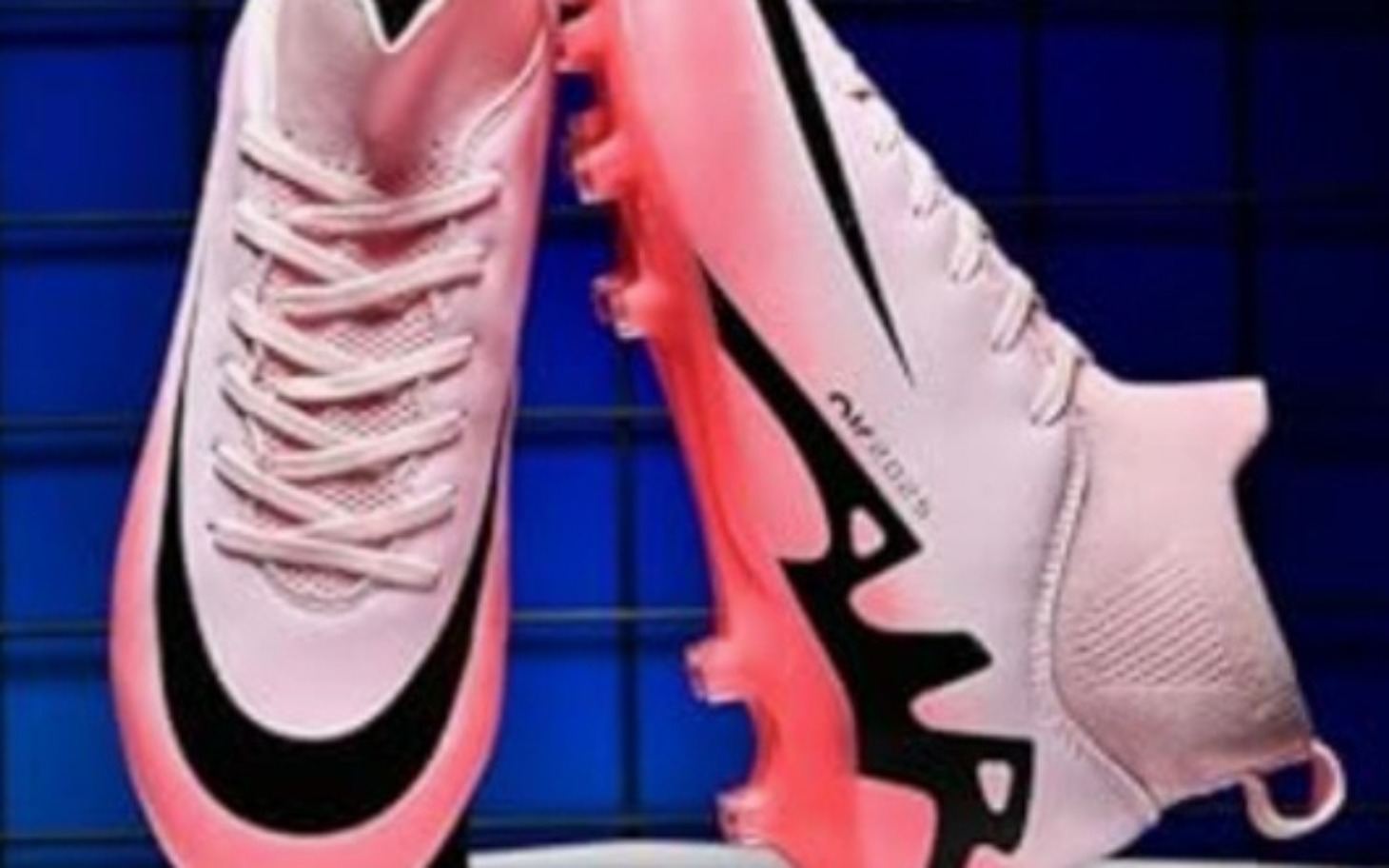 
        Różowe buty piłkarskie Nike na niebieskim tle.
    