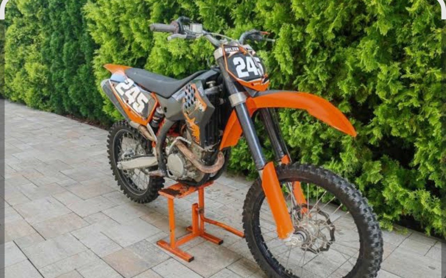 
        Motocykl terenowy, pomarańczowy, na stojaku.
    
