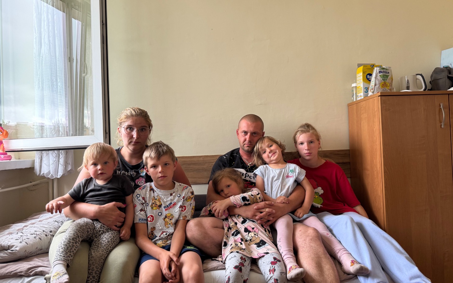
        Rodzina siedząca na łóżku, wspierająca się nawzajem.
    