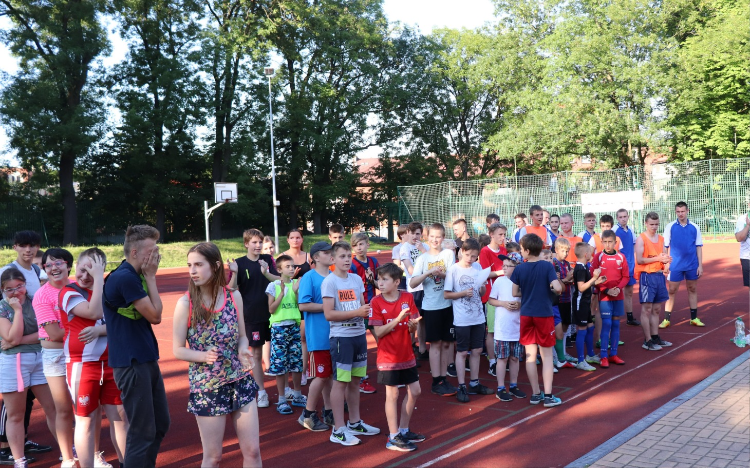 
        Grupa dzieci na boisku sportowym, gotowych do rywalizacji.
    