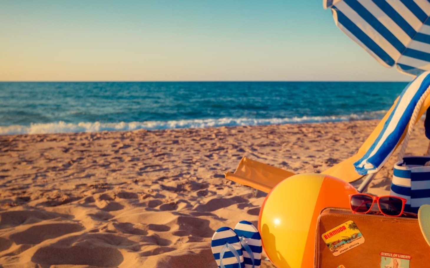 
        Widok na plażę z leżakiem i piłką plażową.
    