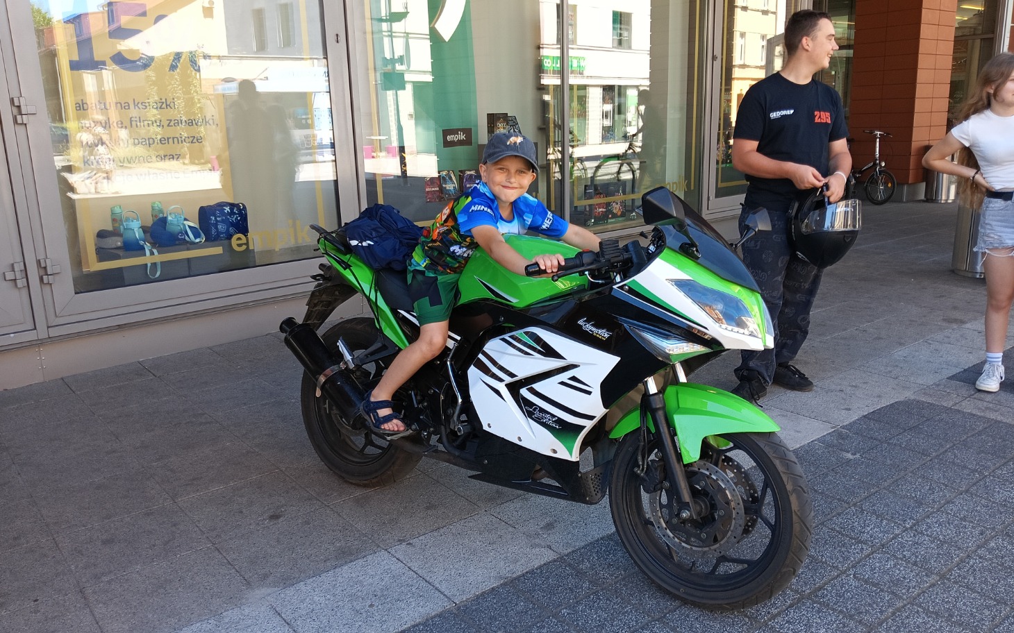 
        Chłopiec na motocyklu, uśmiechający się do kamery.
    
