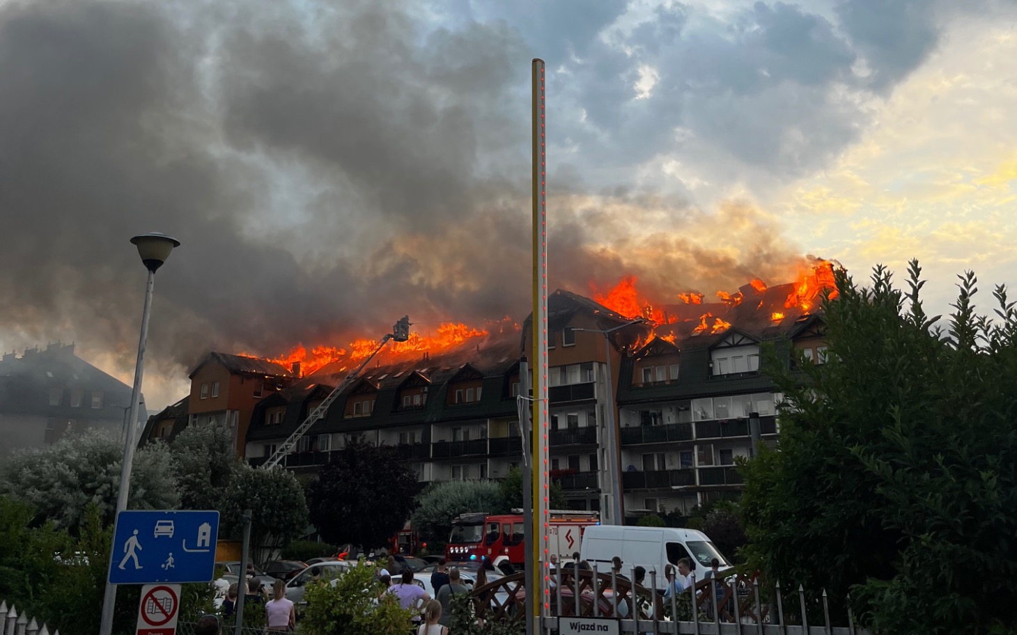 
        Pożar na dachu budynku, ogień i dym w tle.
    