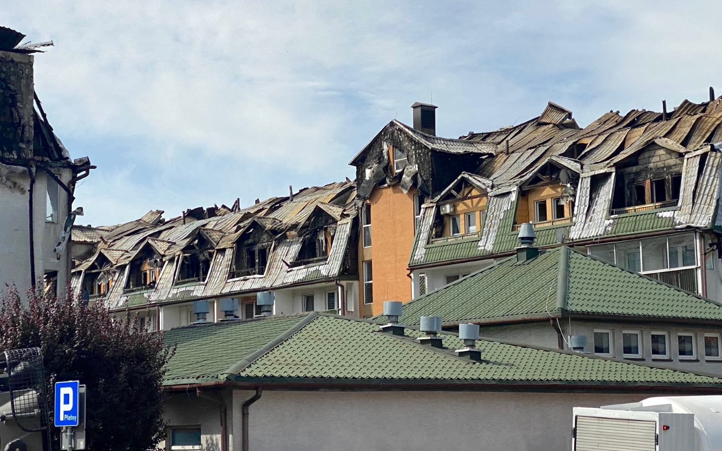 
        Zniszczony dach budynku, widok na uszkodzone okna.
    