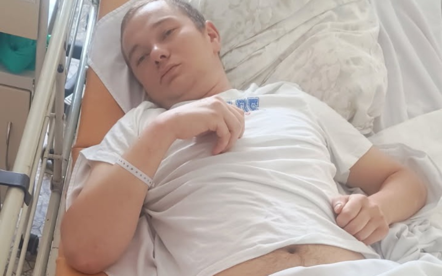 
        Młody mężczyzna leżący w szpitalnym łóżku, wygląda na zmęczonego.
    