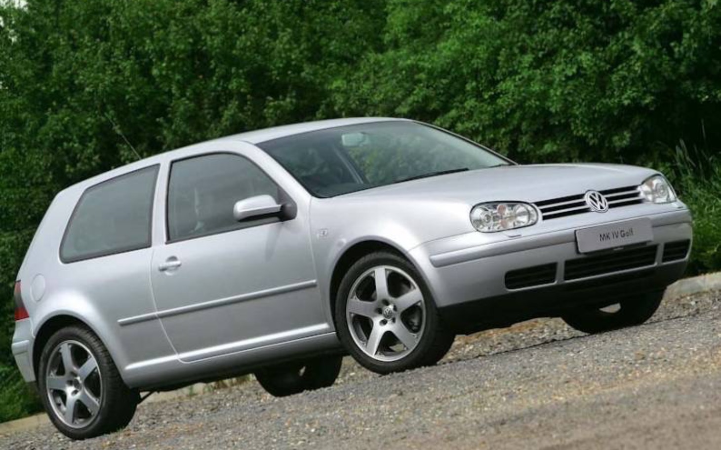 
        Srebrny Volkswagen Golf zaparkowany na drodze w otoczeniu zieleni.
    