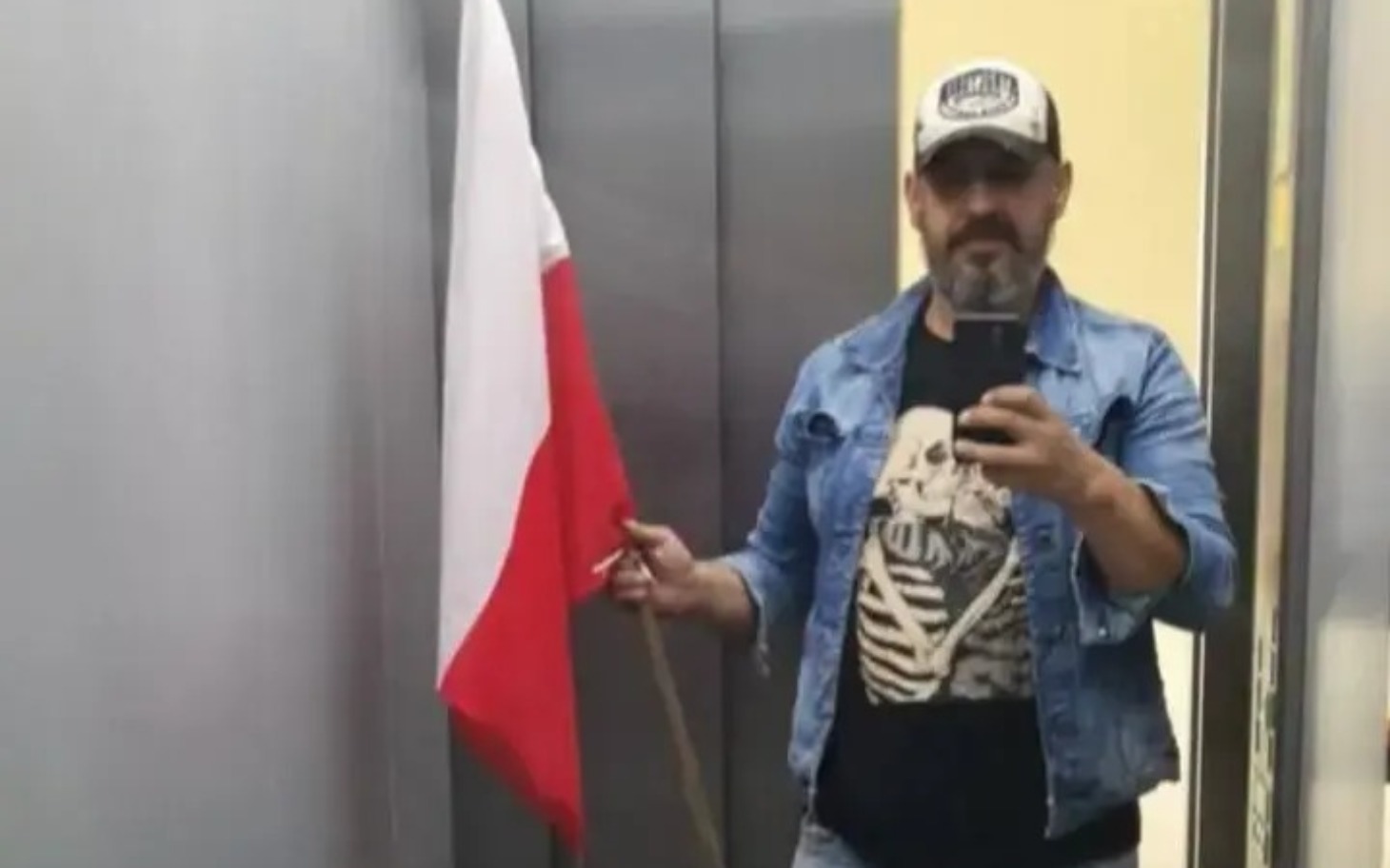 
        Mężczyzna z flagą Polski w windzie.
    