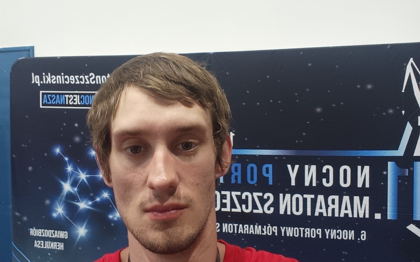
        Mężczyzna na tle plakatu z gwiazdami, w czerwonej koszulce.
    