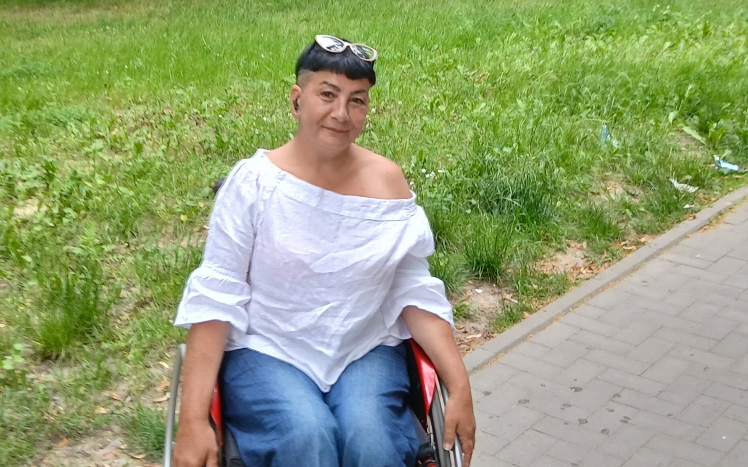 
        Kobieta w wózku inwalidzkim na tle zielonej trawy.
    